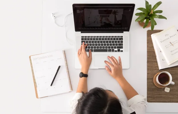 Girl works on macbook along with tea on the right and notes on the left